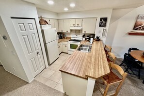 Una cocina compacta con armarios blancos, encimera de madera y comedor con mesa y sillas.