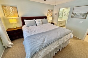 A neatly arranged bedroom with a large bed, bedside tables, a nightstand, and a mirror.