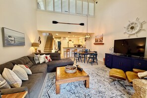 Un salon spacieux, comprenant un canapé, une table basse et un téléviseur. Un escalier mène à l’étage supérieur.