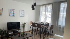 Un salon moderne doté d’un téléviseur à écran plat, d’une table basse et d’un coin repas avec des chaises et une table mise pour le repas.