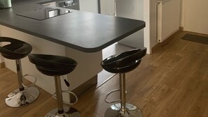 Une cuisine moderne dotée d’un îlot central, de tabourets de bar, d’un four encastré et d’une fenêtre avec des rideaux.