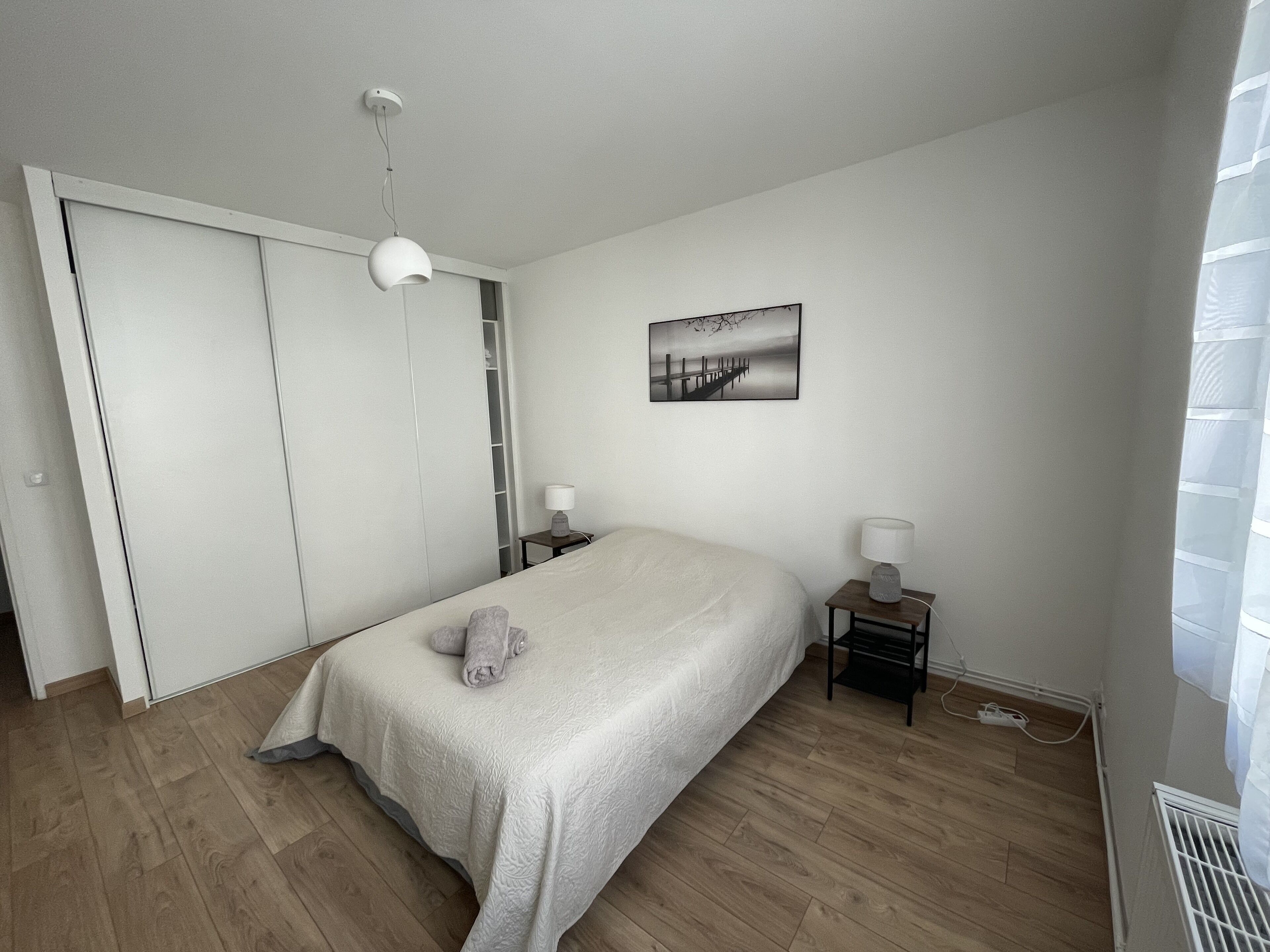 A bedroom with a bed, two bedside tables, a nightstand, a wardrobe, a ceiling light, and a picture on the wall.