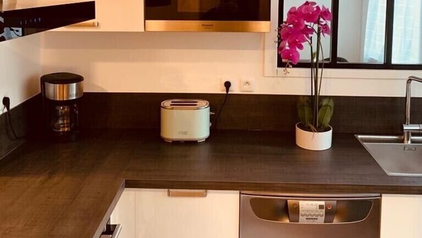 Une cuisine moderne avec des armoires blanches, un four encastré, une machine à café, un grille-pain et une fenêtre offrant une belle vue.