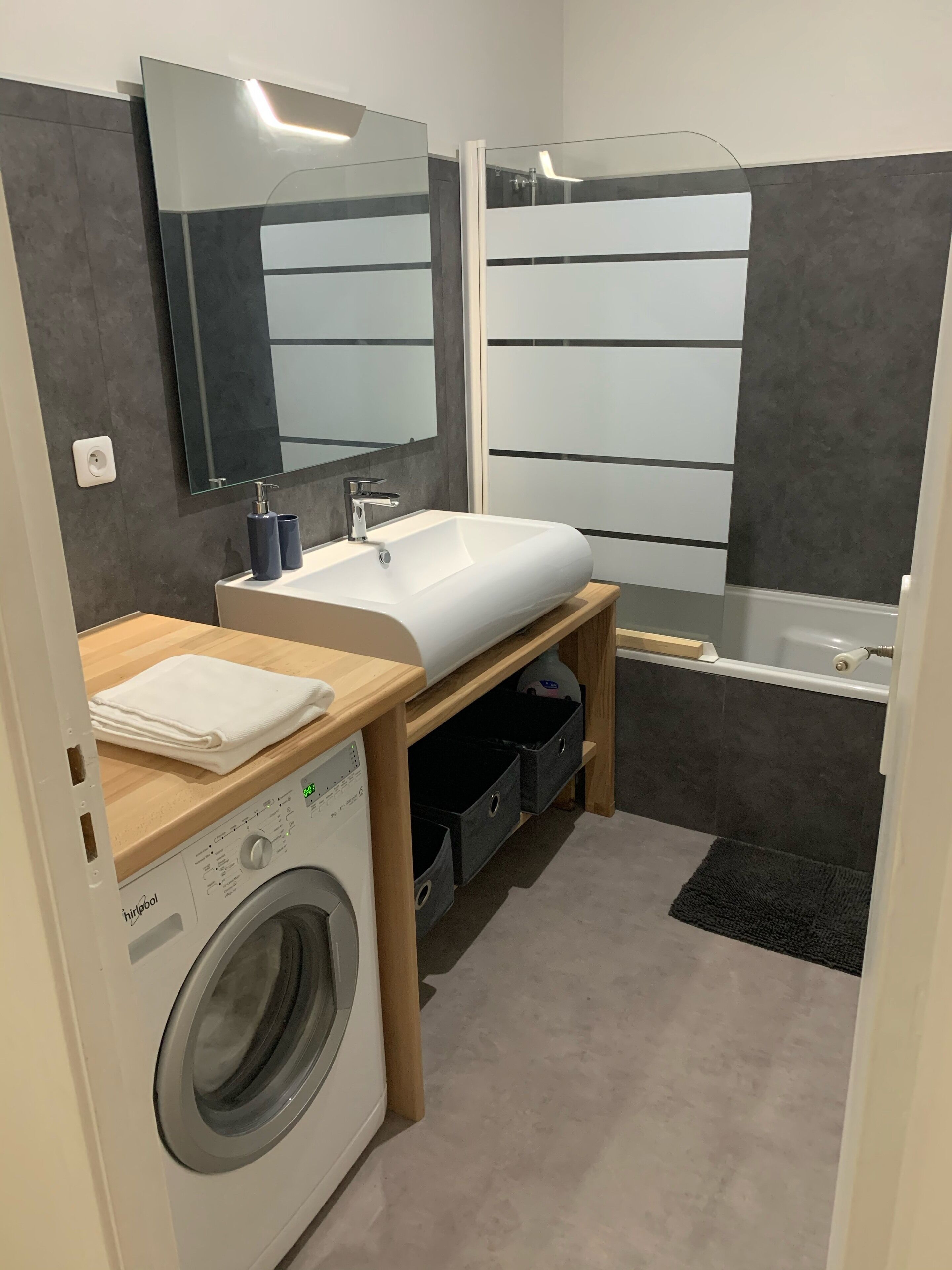 Une petite salle de bain équipée d’un lave-linge, d’un lavabo, d’un miroir et d’une baignoire.