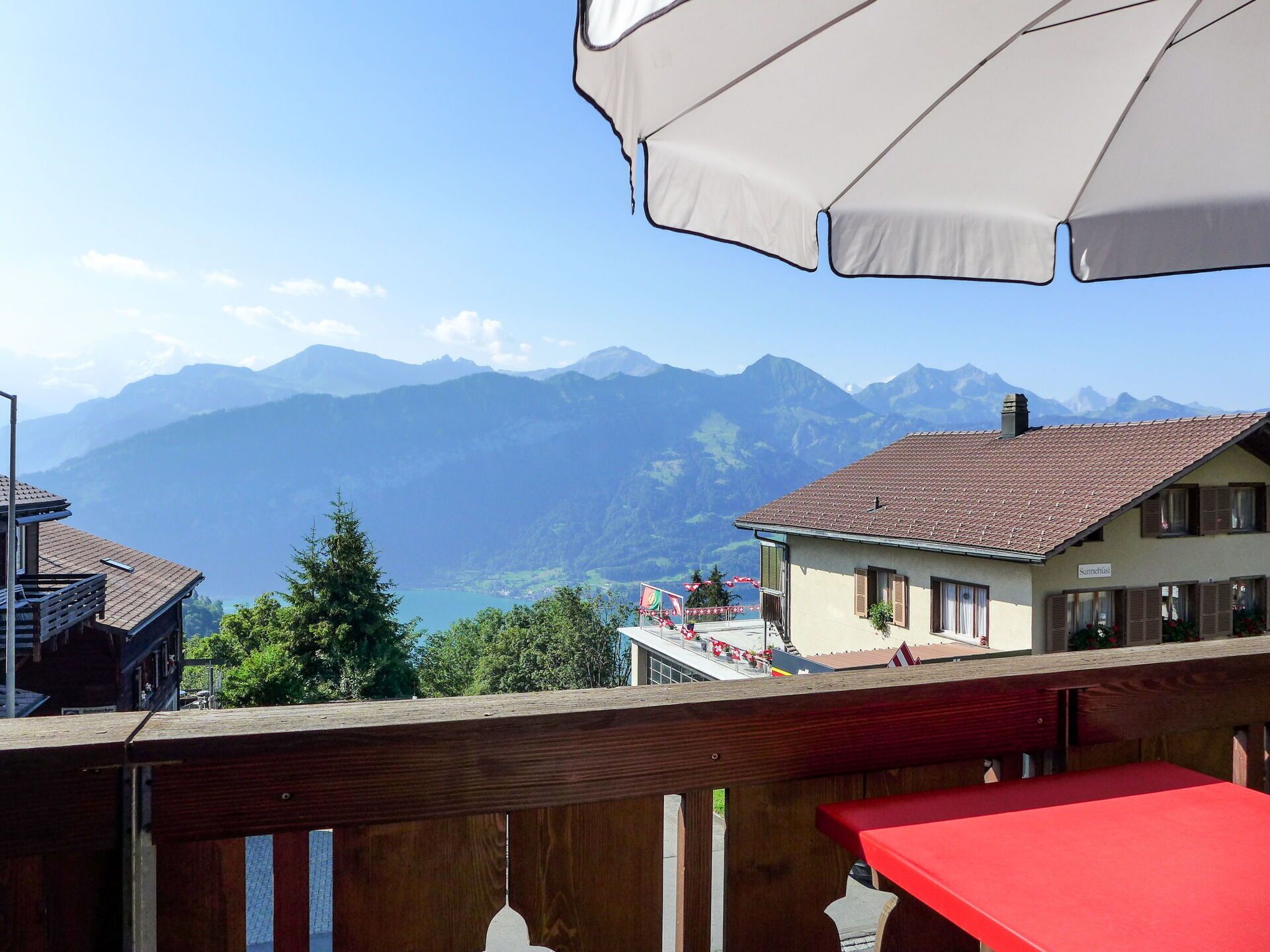 Une vue sur la montagne depuis un balcon, avec une table rouge et un parasol blanc.