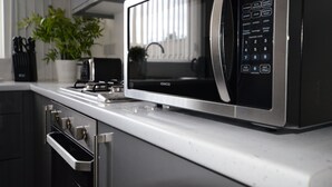 A modern kitchen with a built-in microwave, stainless steel appliances, and a potted plant. - The Prestwood (Wolverhampton)