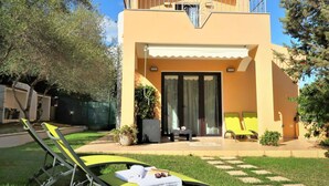 Ein zweigeschossiges Gebäude mit einem Balkon, einer überdachten Terrasse und einer kleinen Sitzgelegenheit im Freien mit Tisch und Stühlen.
