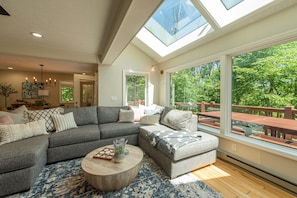 A modern living room with a sectional sofa, a round coffee table, and large windows offering a view of the outdoors.