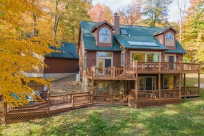 A two-story house with a balcony and a deck, surrounded by autumn foliage.