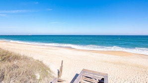 A beach with a wooden walkway leading to the water, a clear sky, and a distant pier.