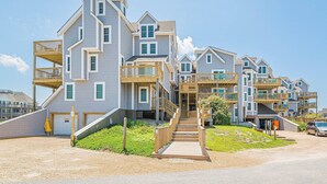 A coastal residential complex with multiple two-story buildings, wooden balconies, and a central staircase leading to a shared entrance.