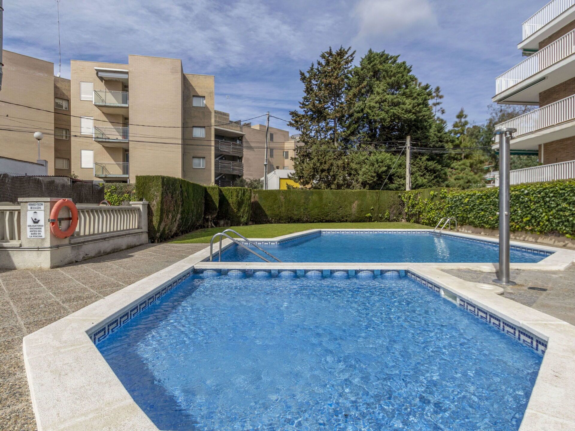 Un espace piscine comprenant deux piscines, entouré d’immeubles d’habitation et de verdure.