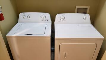 Deux machines à laver à chargement frontal, de couleur blanche, se trouvent dans une buanderie aux murs de couleur beige.