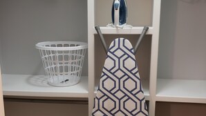 Un área de lavandería con un planchador blanco, una cesta de ropa blanca y un perchero con toallas estampadas.