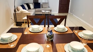 Una mesa de comedor dispuesta con varios platos y vasos, un florero con piedras decorativas, y un sofá al fondo.
