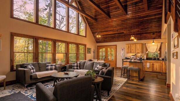 A spacious living area with a large sofa set, a coffee table, and a kitchen area with wooden cabinets and a bar.