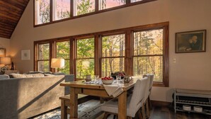 A cozy room with a wooden dining table, a sofa, and large windows with a forest view.