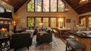 A cozy interior with a fireplace, large windows, a dining area, and a kitchen.