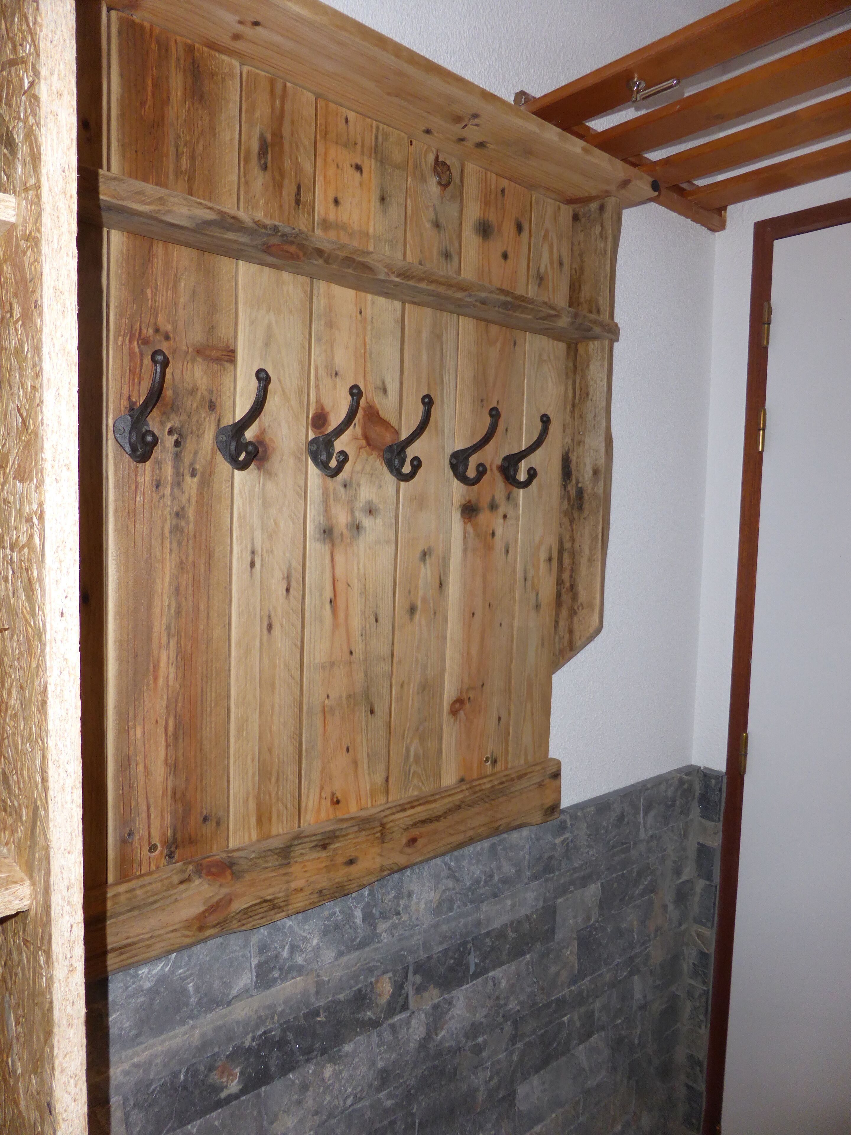 A wooden wall with five metal hooks.