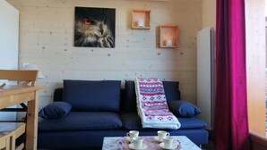 A cozy living room with a dark blue sofa, a coffee table with cups, a painting of an owl, and a wooden wall. - SOUTH ALPES APARTMENT PUY SAINT VINCENT 1800 M Ski resort summer / winter (Puy-Saint-Vincent)