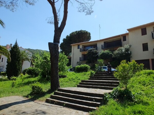 A set of stone steps leading up to a building with multiple balconies, surrounded by greenery and a clear sky.