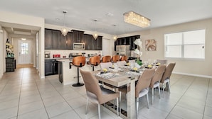 A modern kitchen with dark cabinets, a central island, and a dining area with a large table and chairs.