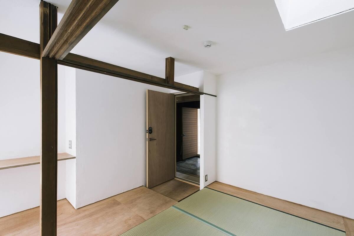 A room with a wooden floor, a tatami mat, a sliding door, and a view into another room with a sliding door.