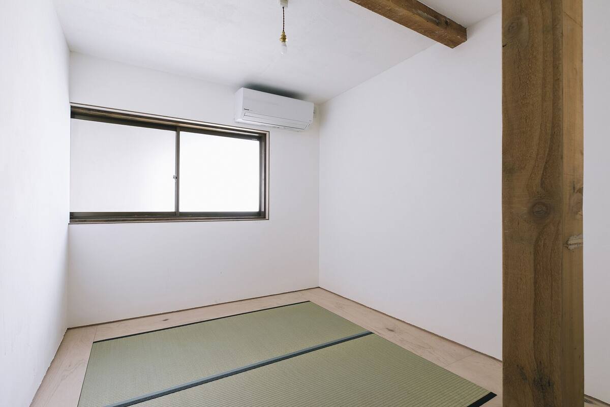 A room with a tatami mat floor, a window with a metal frame, and a ceiling-mounted air conditioning unit.