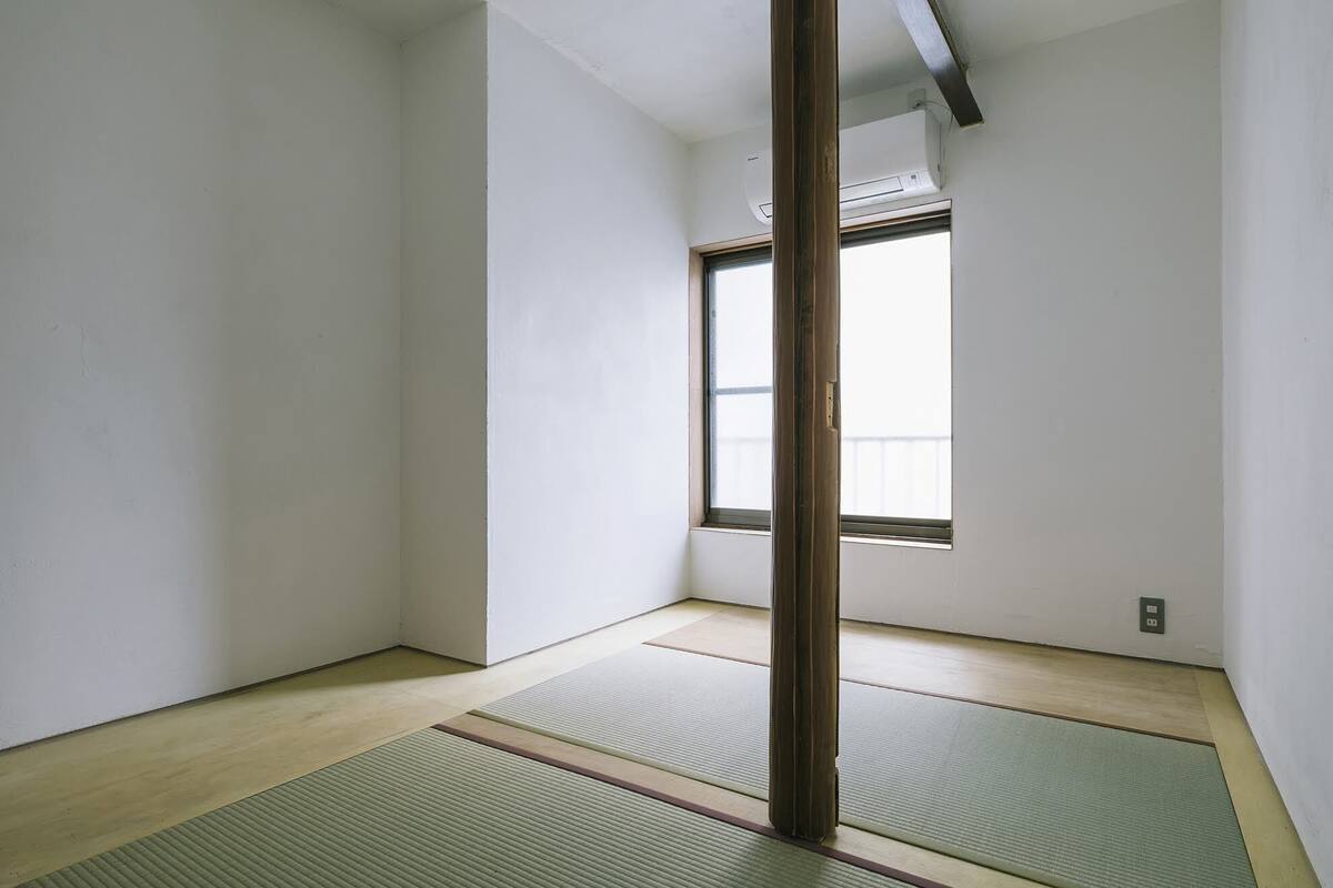A room with tatami mats, a wooden pillar, and a window with a view of a balcony.