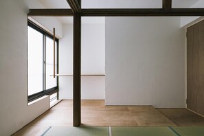 Una habitación minimalista con un ventanal grande, vigas de madera y suelo de tatami.