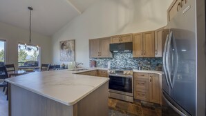 Una cocina moderna con una isla grande, horno empotrado, refrigerador de acero inoxidable y armarios de madera.