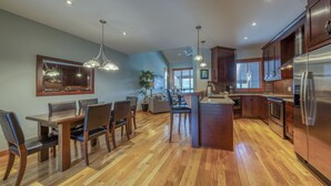 Una cocina moderna con armarios de madera, electrodomésticos de acero inoxidable y una zona de comedor con mesa y sillas de madera.