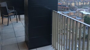 Ein Balkon mit Blick auf eine Stadtlandschaft, mit einer schwarzen Wand und einem Stuhl.