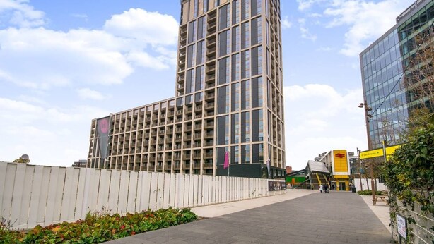 Ein modernes Hochhaus mit einer gitterförmigen Fassade, einem Fußweg davor und blauem Himmel.