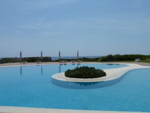A swimming pool with lounge chairs and umbrellas, surrounded by greenery and a view of the sea. - Villa ORIOL (Es Canutells)