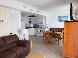 A compact living space with a kitchenette, a brown sofa, a wooden dining table, and a TV mounted on a wooden cabinet. - Beachfront 1bd Condo-Huge Balcony Looking Directly at Beach (South Padre Island)