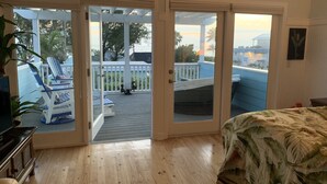 Een kamer met een houten vloer, een bed met een bloemenprint en uitzicht op een terras met stoelen en een hangmat.