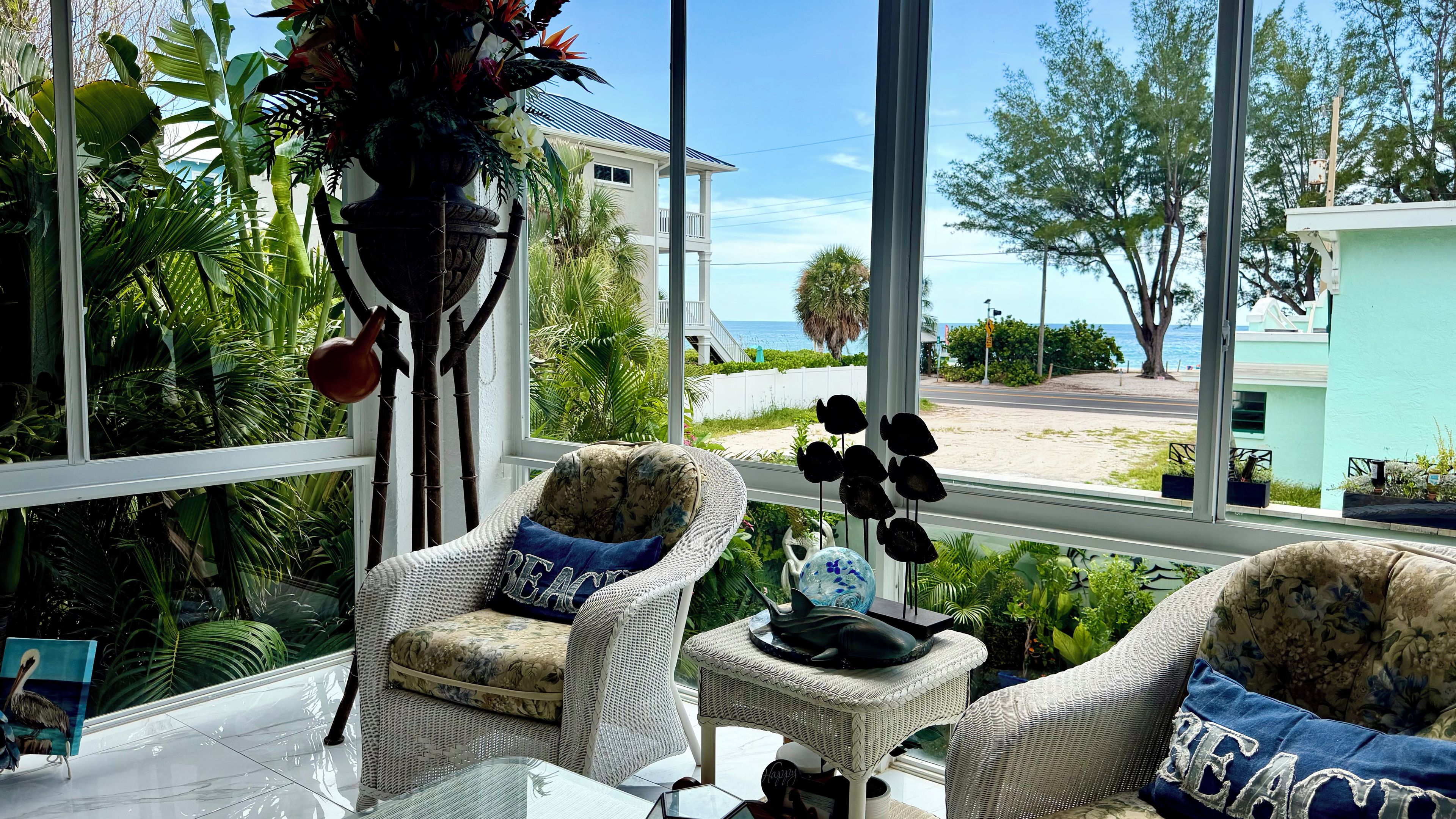 A room with two wicker chairs, a table, and a view of the beach.