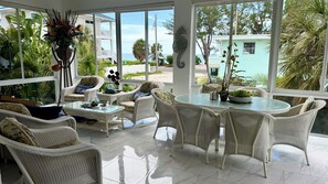 A sunlit room with wicker furniture, a glass coffee table, and a view of the ocean.