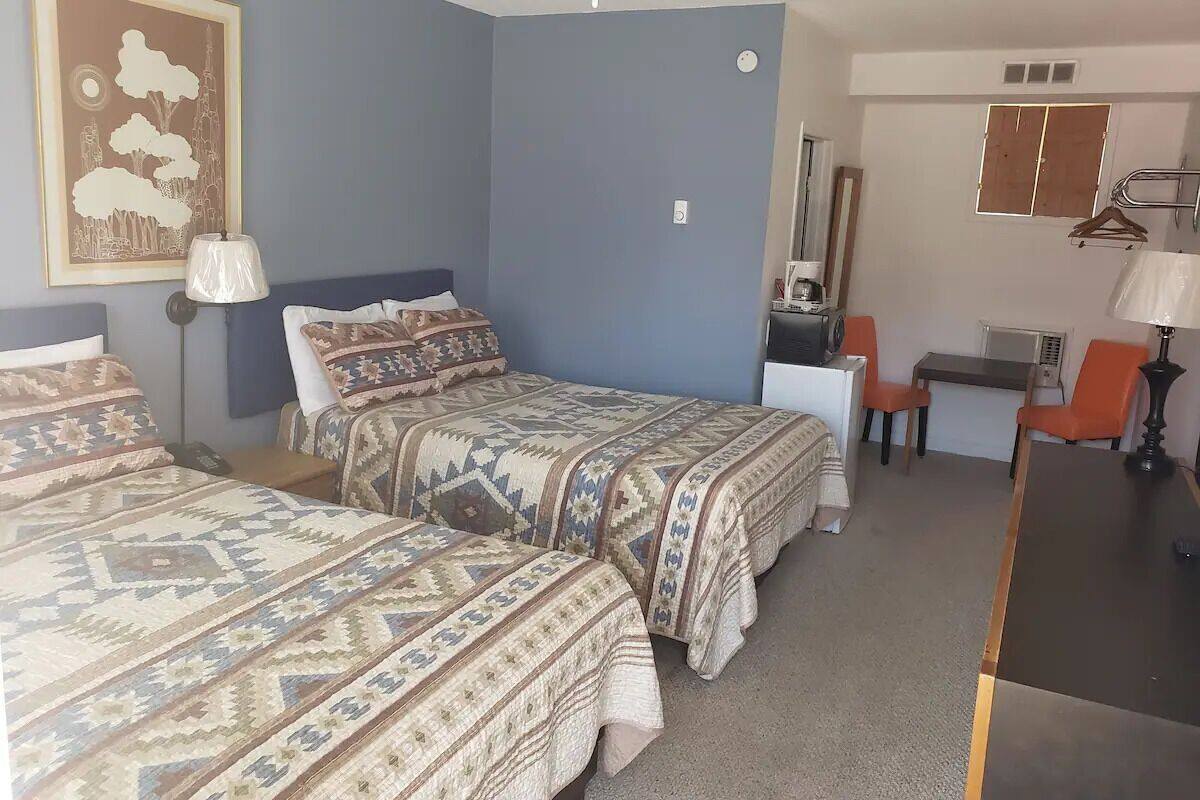 A room with two beds, a desk, a chair, and a hanging coat rack.