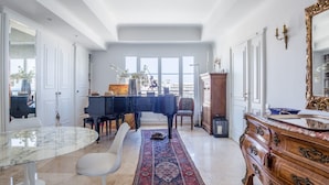 A spacious living room with a grand piano, a marble coffee table, and a large ornate dresser. - Art Deco Luxury Apartment (Cannes)