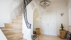 A grand staircase with a black wrought iron railing, a chandelier, and a white door with a small potted cactus beside it. - Art Deco Luxury Apartment (Cannes)