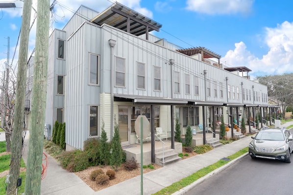 A modern multi-story residential building with a covered front porch and a car parked in front.