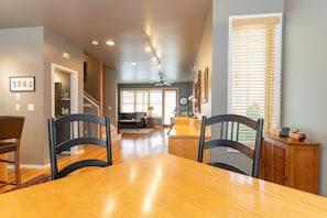 A dining area with a wooden table and chairs, a kitchen in the background, and a staircase leading to another level.
