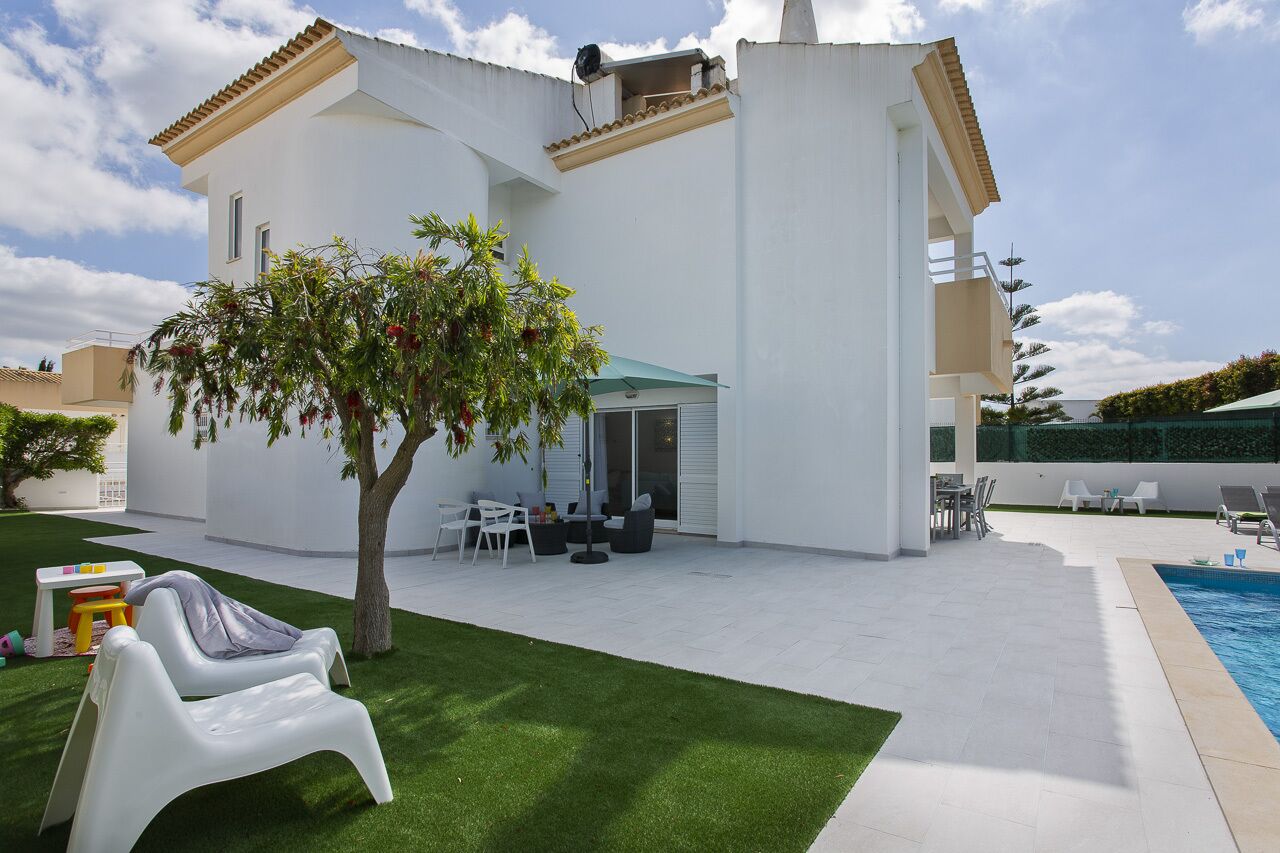 Ein modernes Haus mit Swimmingpool, einer Terrasse mit Gartenmöbeln und einem gepflegten Rasen.