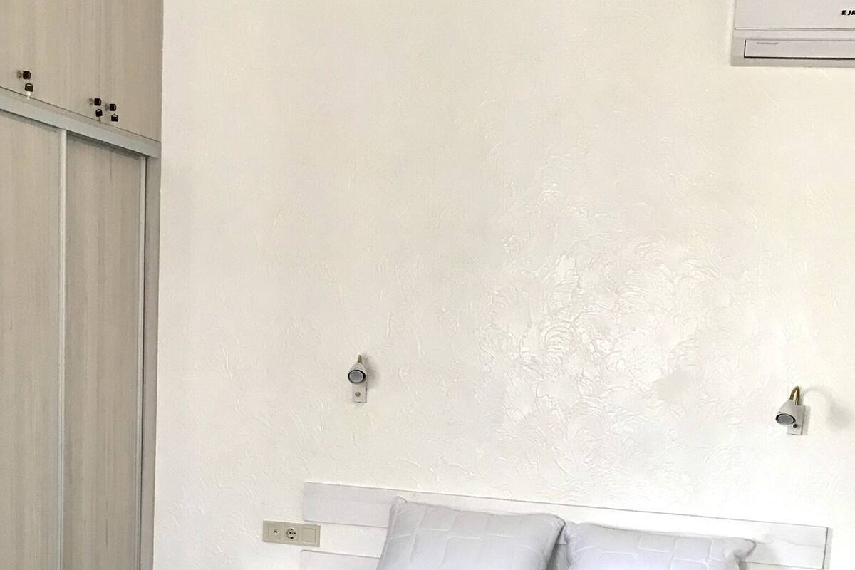 Ein Schlafzimmer mit einem Bett, weißen Nachttischen, einem Kleiderschrank und einer Wandleuchte.