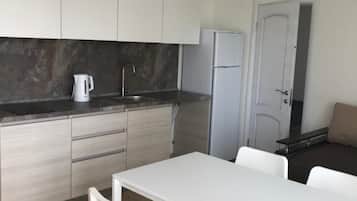 A modern kitchen with white cabinets, a black countertop, a white dining table with chairs, and a refrigerator.