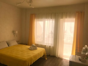 A hotel room with a bed, a nightstand, a lamp, and a window with curtains.