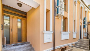 Um edifício com porta de madeira, um conjunto de degraus que levam à entrada e aparelhos de ar condicionado fixados na parede externa.