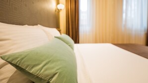 Uma cama bem arrumada com almofadas brancas e verdes, uma cabeceira com padrão geométrico e uma luminária fixada na parede.